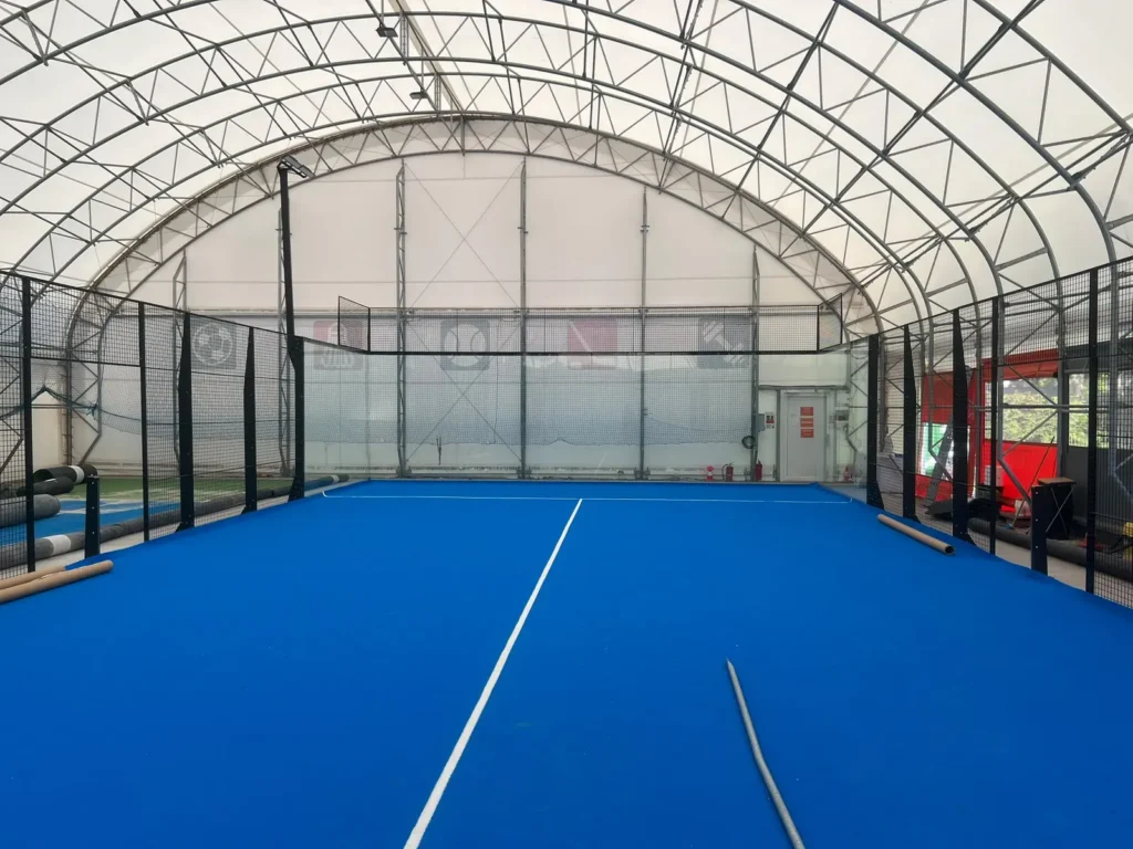 Padelový kurt v krytej hale FitCamp v bratislavskom Ružinove počas montáže, modrý hrací povrch a sklenené steny