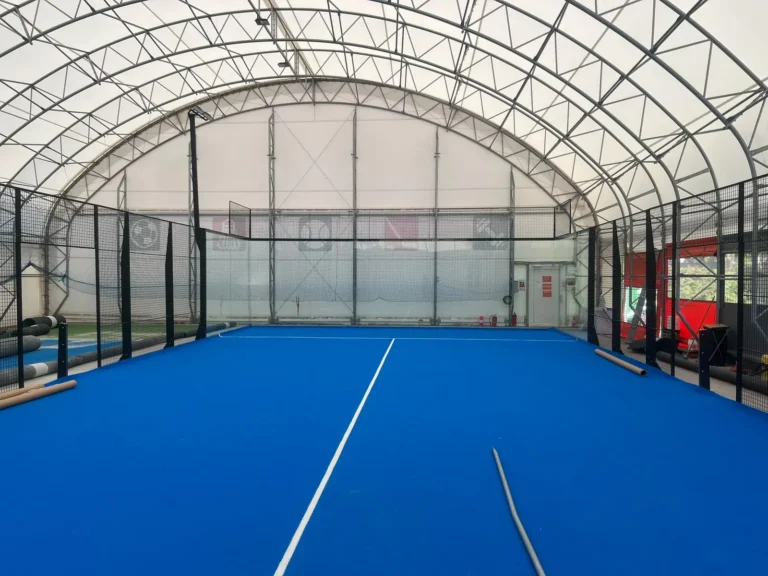 Padelový kurt v krytej hale FitCamp v bratislavskom Ružinove počas montáže, modrý hrací povrch a sklenené steny
