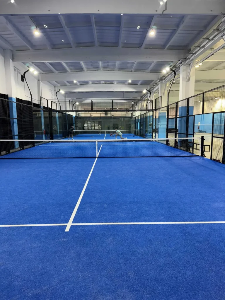 Kryté padelové kurty v hale Racket Arena v Žiline s modrým povrchom, v pozadí hráči počas zápasu